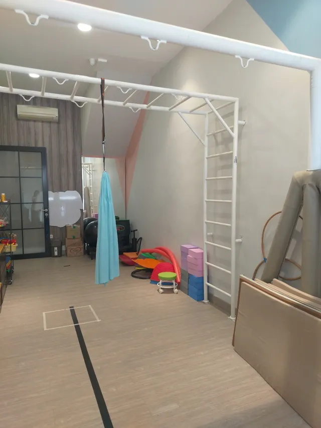 Room with a white overhead frame, mats, and play equipment