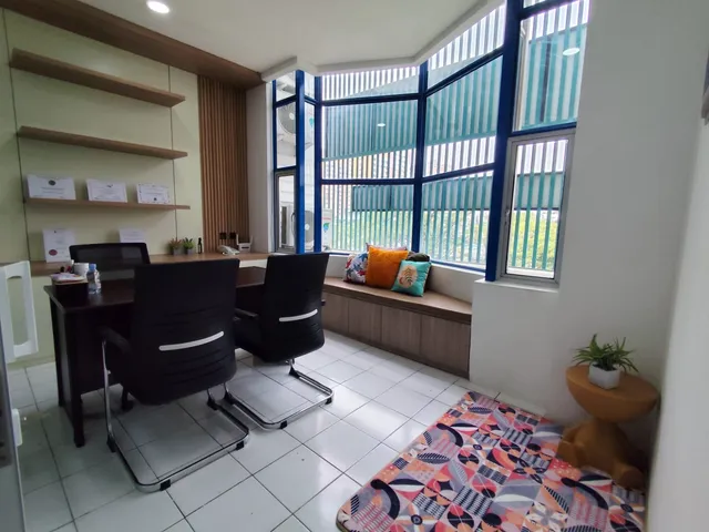 Room with a desk, black chairs, a window bench with colorful cushions, and a patterned sofa