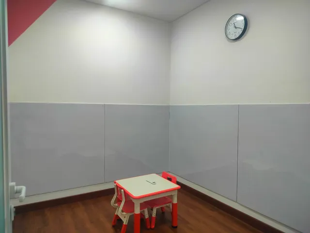 Room with a wooden floor, a small red-edged table, two small chairs, and gray wall panels